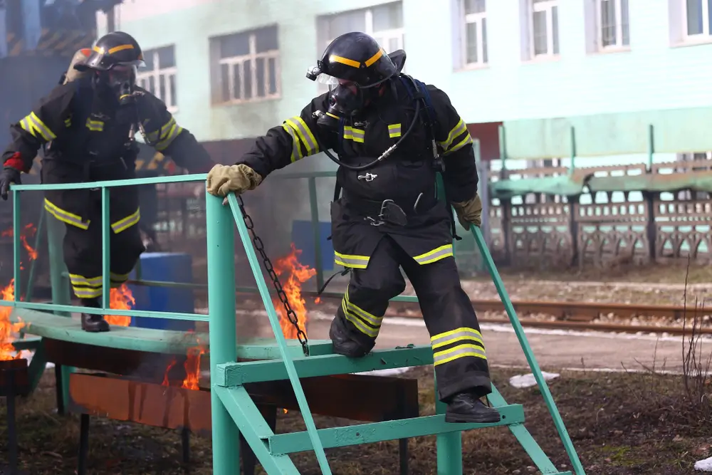 Pompier franchissant une structure au-dessus de flammes lors d'un entraînement sur un parcours d'obstacles.