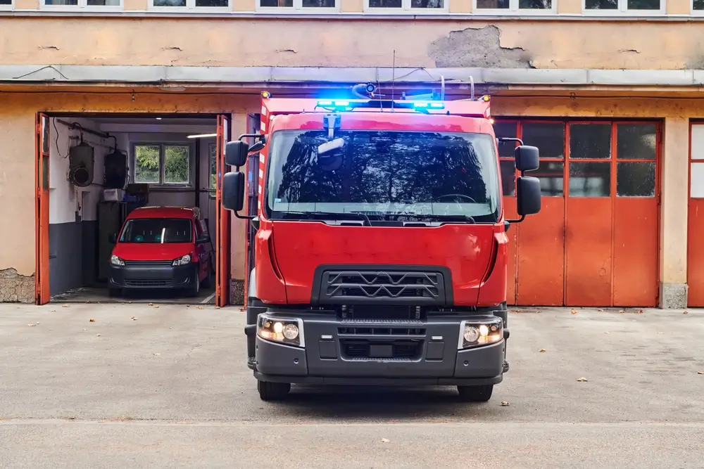 Camion de pompiers stationné devant les garages d'une école du feu avec ses gyrophares bleus allumés.