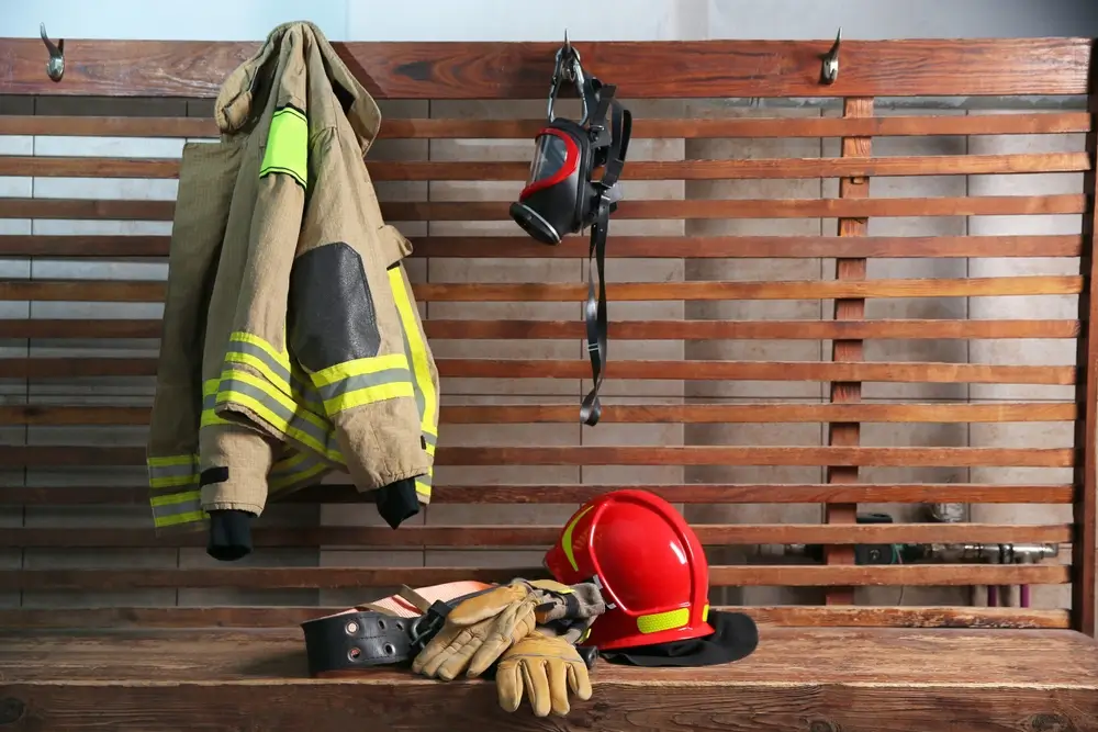 Tenue de pompier avec veste, casque rouge et gants d'intervention disposés sur un banc dans une caserne.