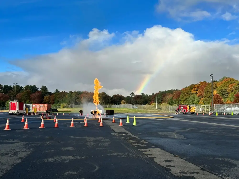 Terrain d'entraînement d'une école du feu avec jet de flammes, cônes de signalisation et camion de pompiers.