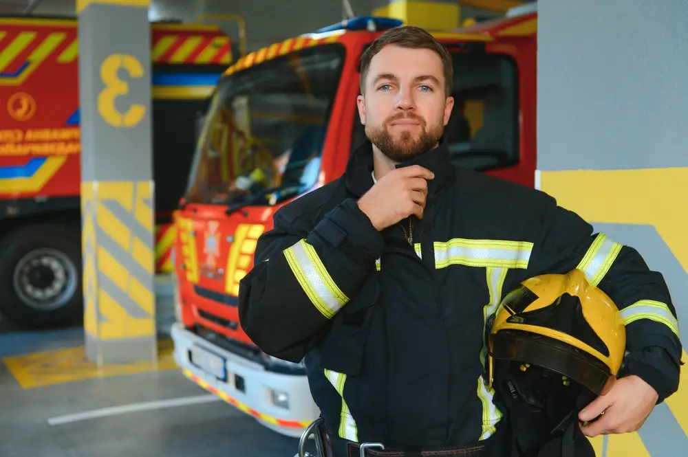 Pompier en uniforme tenant son casque devant un camion de secours stationné dans le garage d'une caserne.