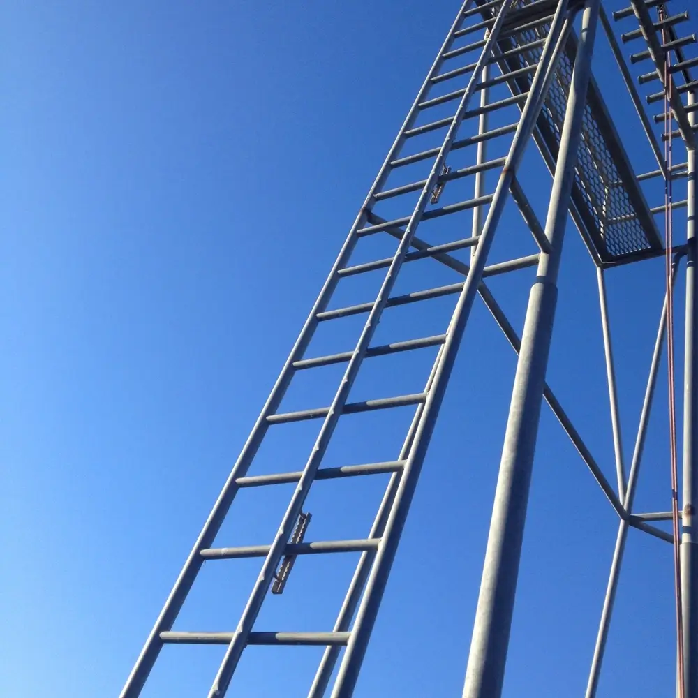 Échelle métallique d'une tour d'entraînement pour pompiers s'élevant vers un ciel bleu au centre de formation.