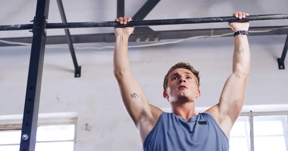 Jeune homme utilisant une barre de tractions en salle de musculation dans le cadre de sa préparation physique.