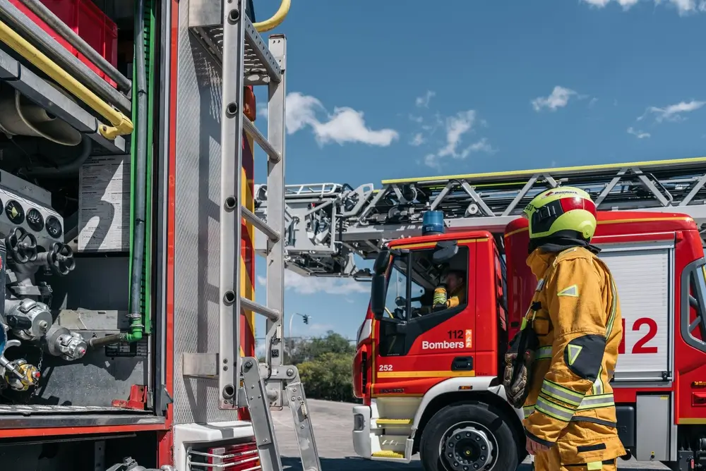 Pompier en tenue d’intervention et véhicules de secours dans la cour d’une caserne de pompiers.