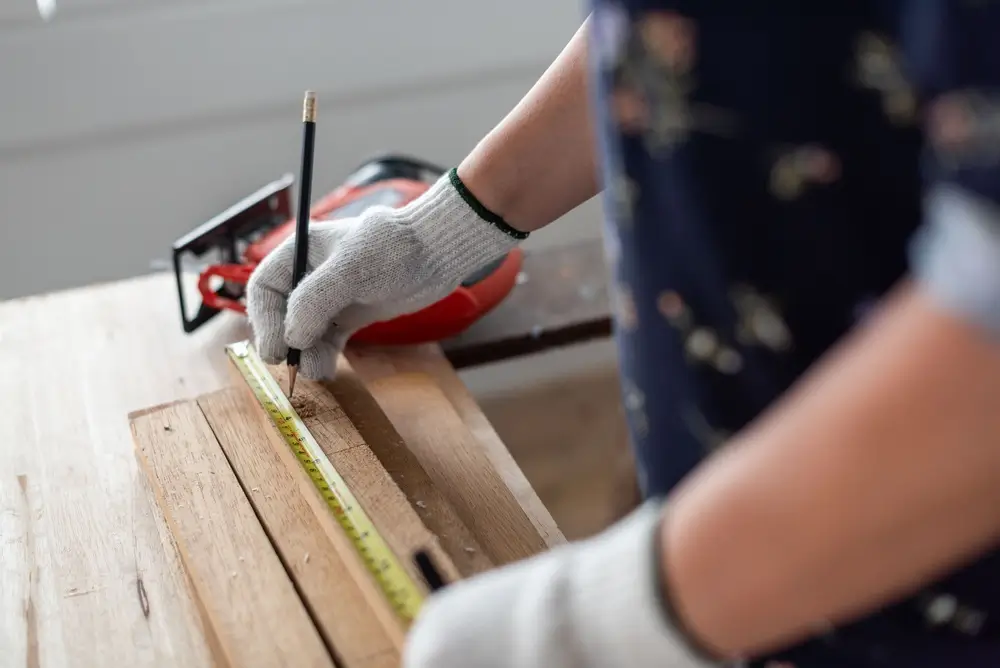 Personne mesurant du bois avec un mètre ruban et un crayon pour ses travaux de bricolage et menuiserie à la maison.