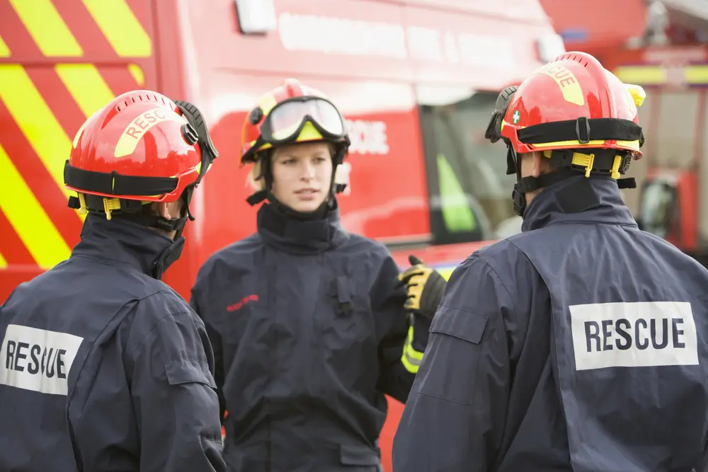 Trois pompiers lors d'un briefing devant leur véhicule en caserne, illustrant la préparation des cadres opérationnels.