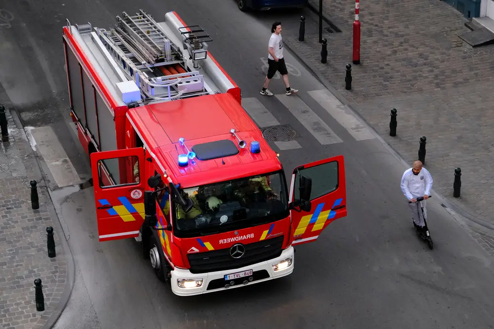 Pompiers belges en uniforme d'intervention à l'intérieur d'un camion de secours rouge en mission urbaine.