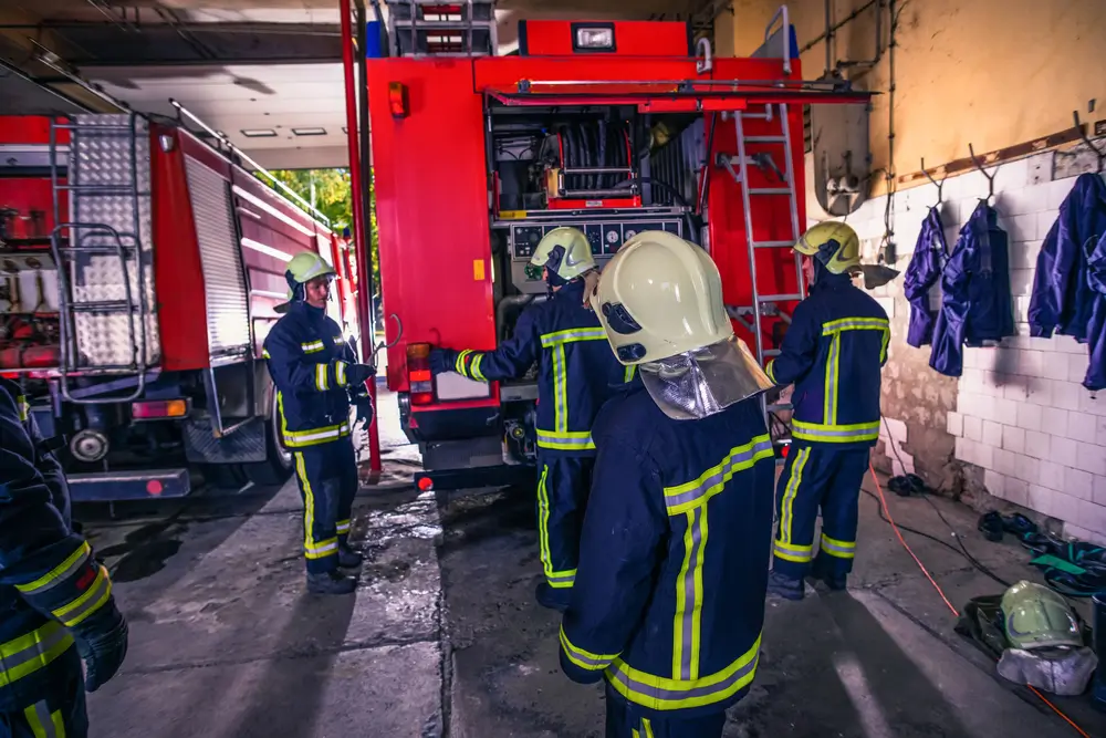 Pompiers professionnels inspectant le matériel à l'arrière d'un camion d'incendie rouge au sein d'une caserne.
