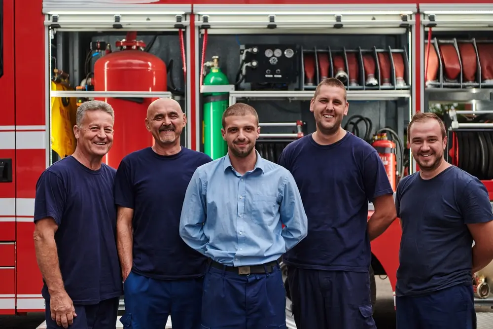 Groupe de recrues pompiers souriant devant un camion d'intervention lors de leur formation à la sécurité collective.