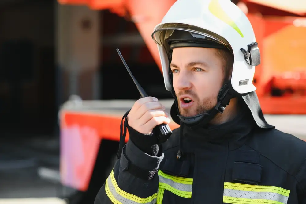 Officier pompier en casque blanc utilisant sa radio pour assurer le commandement lors d'une intervention incendie.