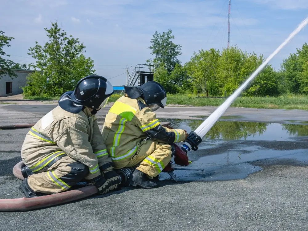 Deux pompiers s'entraînent à manipuler une lance à eau lors d'un exercice de formation aux manœuvres de secours.