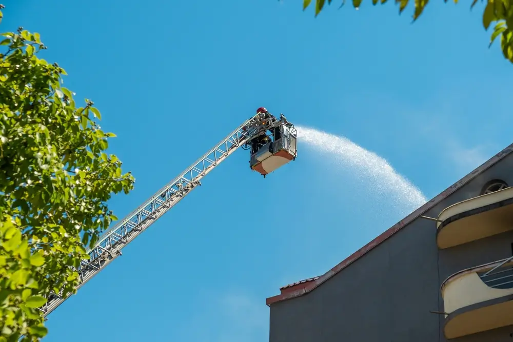 Sapeur-pompier sur une grande échelle projetant de l'eau sur un bâtiment lors d'un entraînement physique opérationnel.