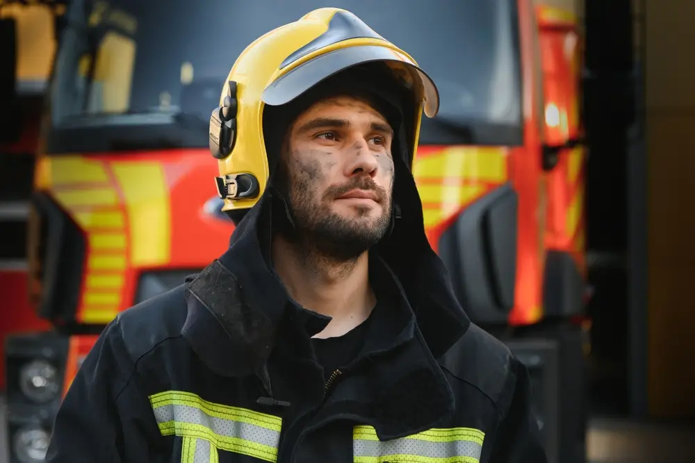 Portrait d'un pompier belge au visage noirci devant son camion d'intervention dans une caserne de pompiers.