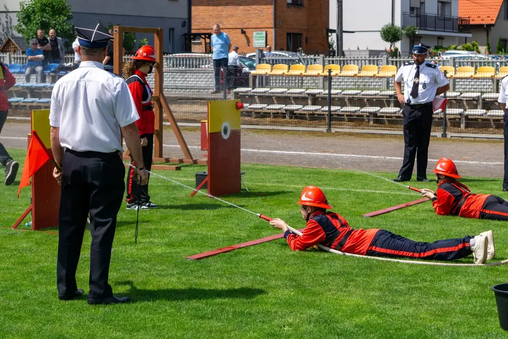 Jeunes cadets pompiers en exercice de manipulation de lance à incendie, visant une cible sous l'œil des instructeurs.