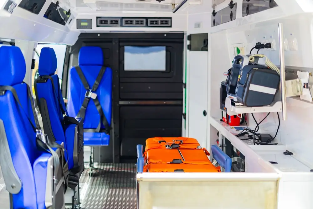 Intérieur d'une ambulance équipée avec brancard orange, sièges bleus et matériel médical pour les soins d'urgence.