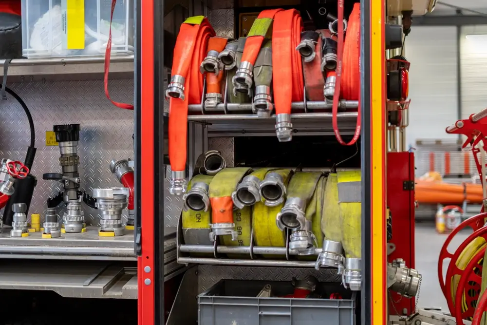 Tuyaux d'incendie enroulés et lances à eau rangés dans les compartiments métalliques d'un camion de pompier.
