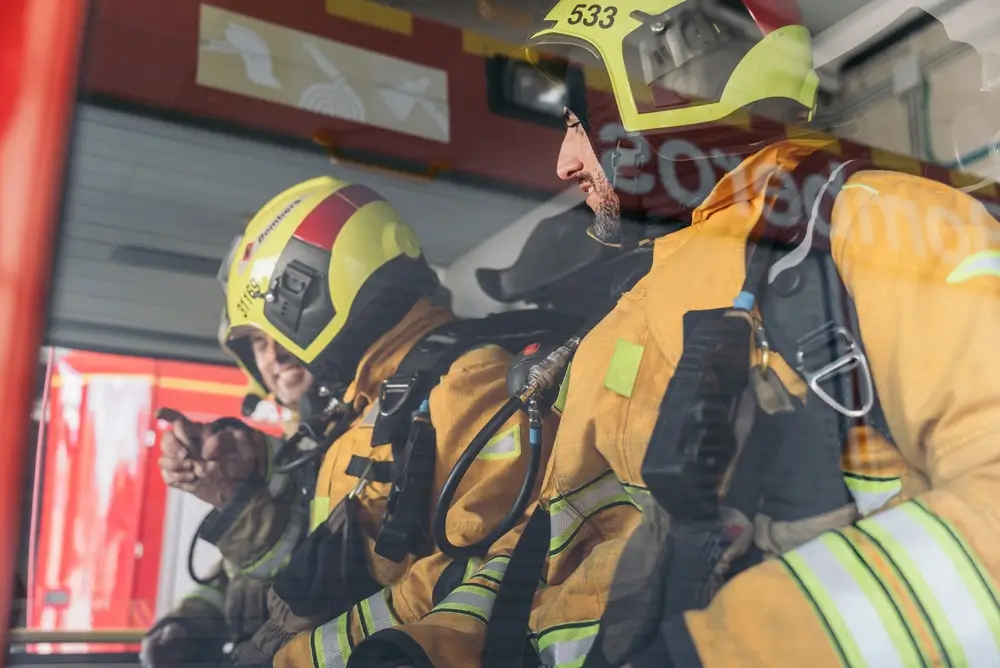 Pompiers professionnels en tenue d'intervention discutant dans leur véhicule de secours au sein d'une caserne.