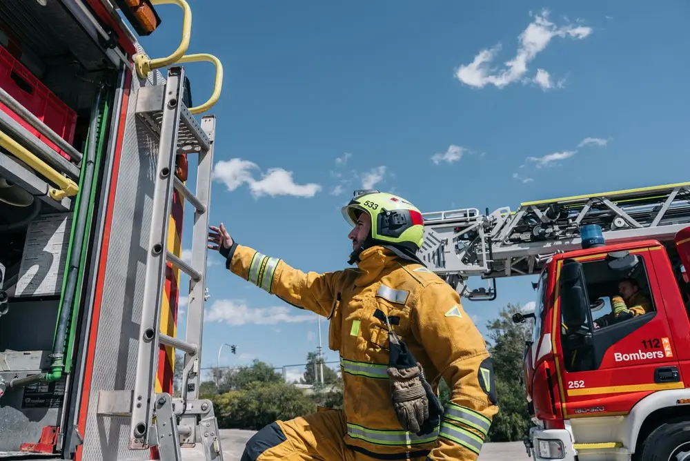 Pompier en tenue jaune manipulant une échelle sur un camion lors d'un entraînement de formation incendie.