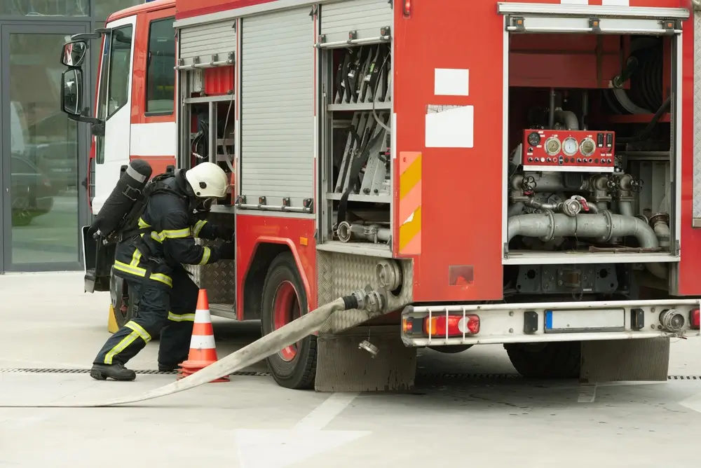 Pompier belge en tenue d'intervention inspectant un camion d'incendie devant une caserne de secours.