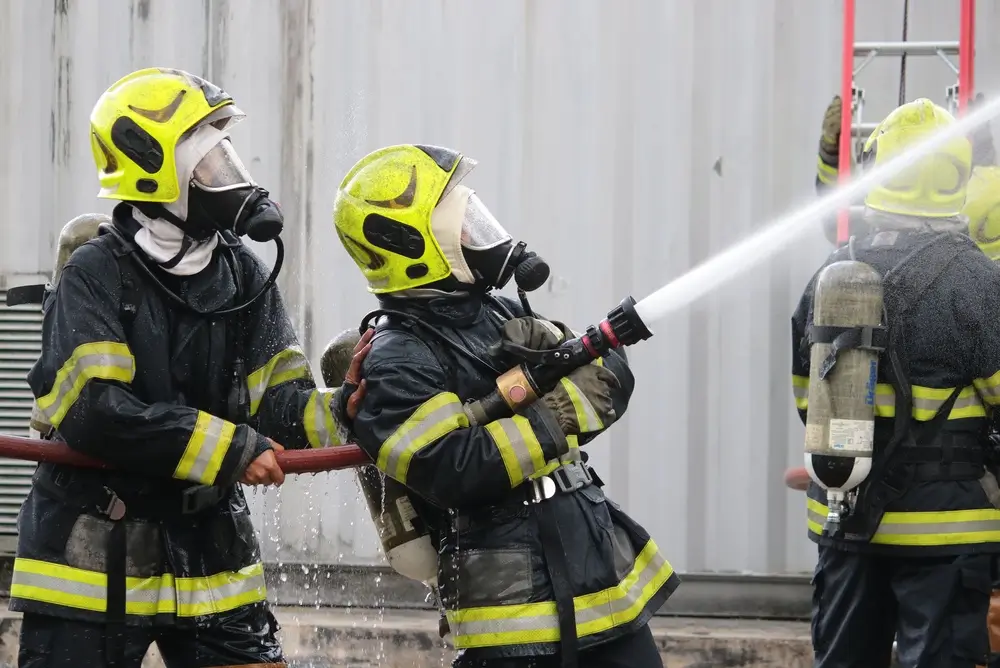 Équipe de pompiers en plein entraînement maniant une lance. Leurs casques permettent d'identifier les différents grades.