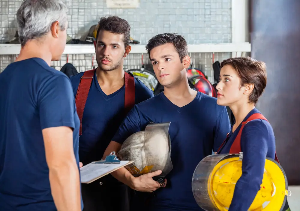 Trois pompiers écoutent attentivement le briefing de leur officier dans une caserne avant une mission d'urgence.